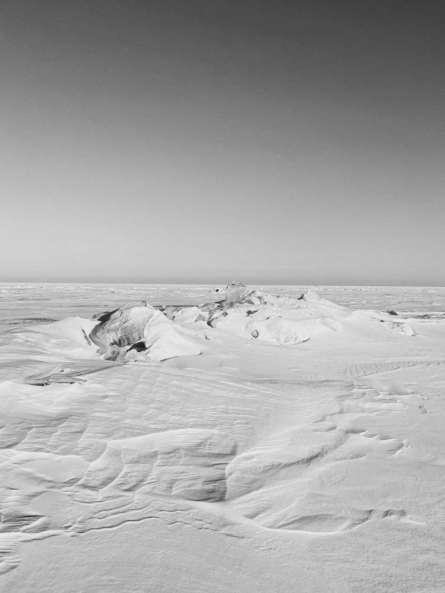 Black and white photograph of snow drifts and ice formations on a frozen lake